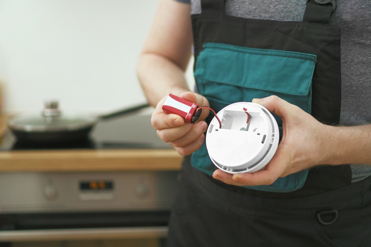 A person is taking the battery out of a smoke alarm.