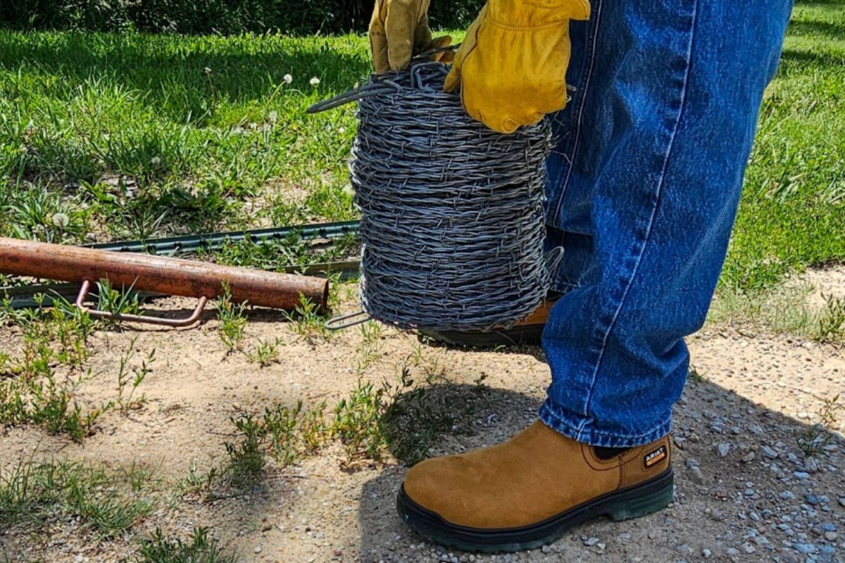 Person wearing yellow work boots with yellow work gloves holding barbed wire