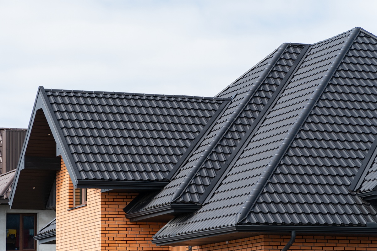 A red brick home with a black metal roof fashioned into a shingle shape. 