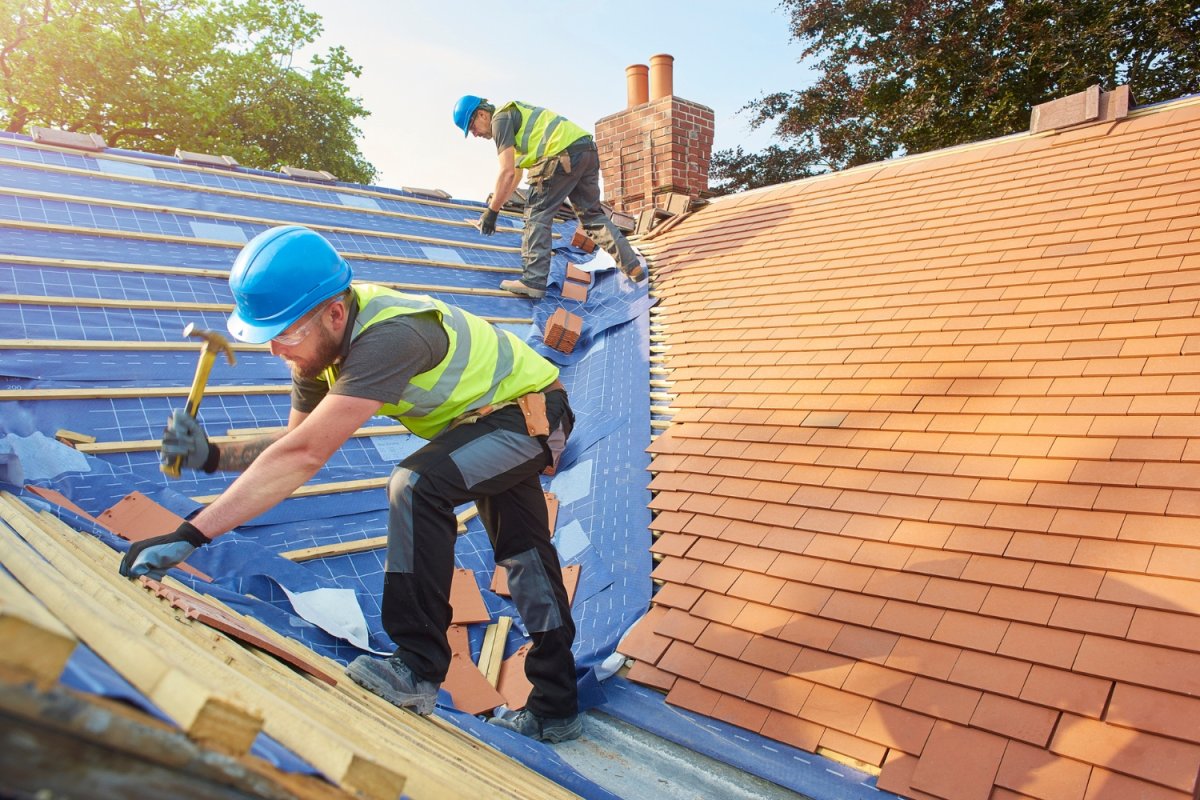 Two roofers in blue hard hats and yellow vest install a roof.