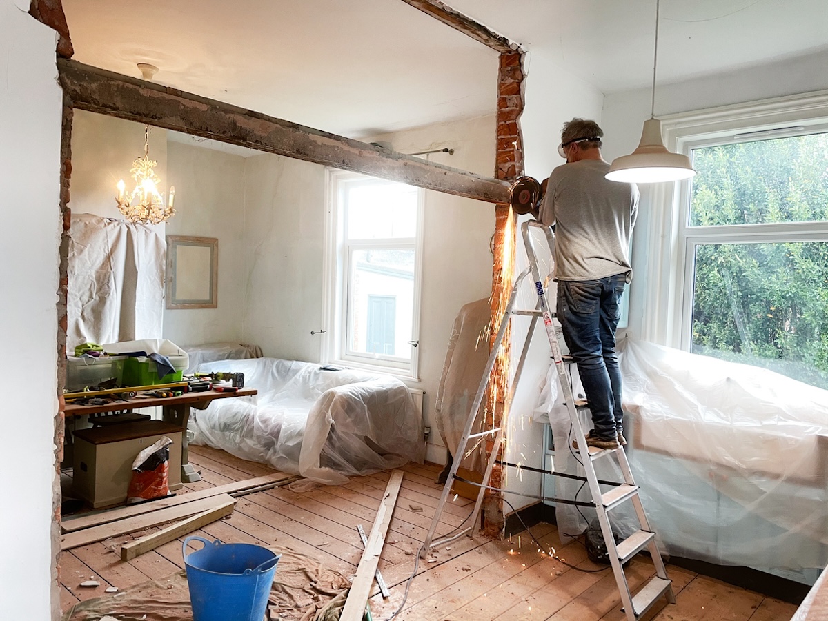 Person demolishing a wall with plastic wrap on furniture.