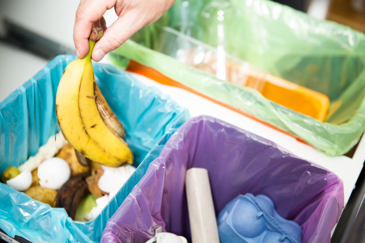 close overhead view of garbage cans and recycling in kitchen draw with hand tossing out banana peel