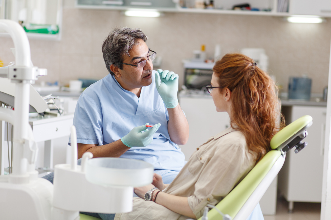 Dentiste senior dans un cabinet dentaire discutant avec une patiente et se préparant au traitement.