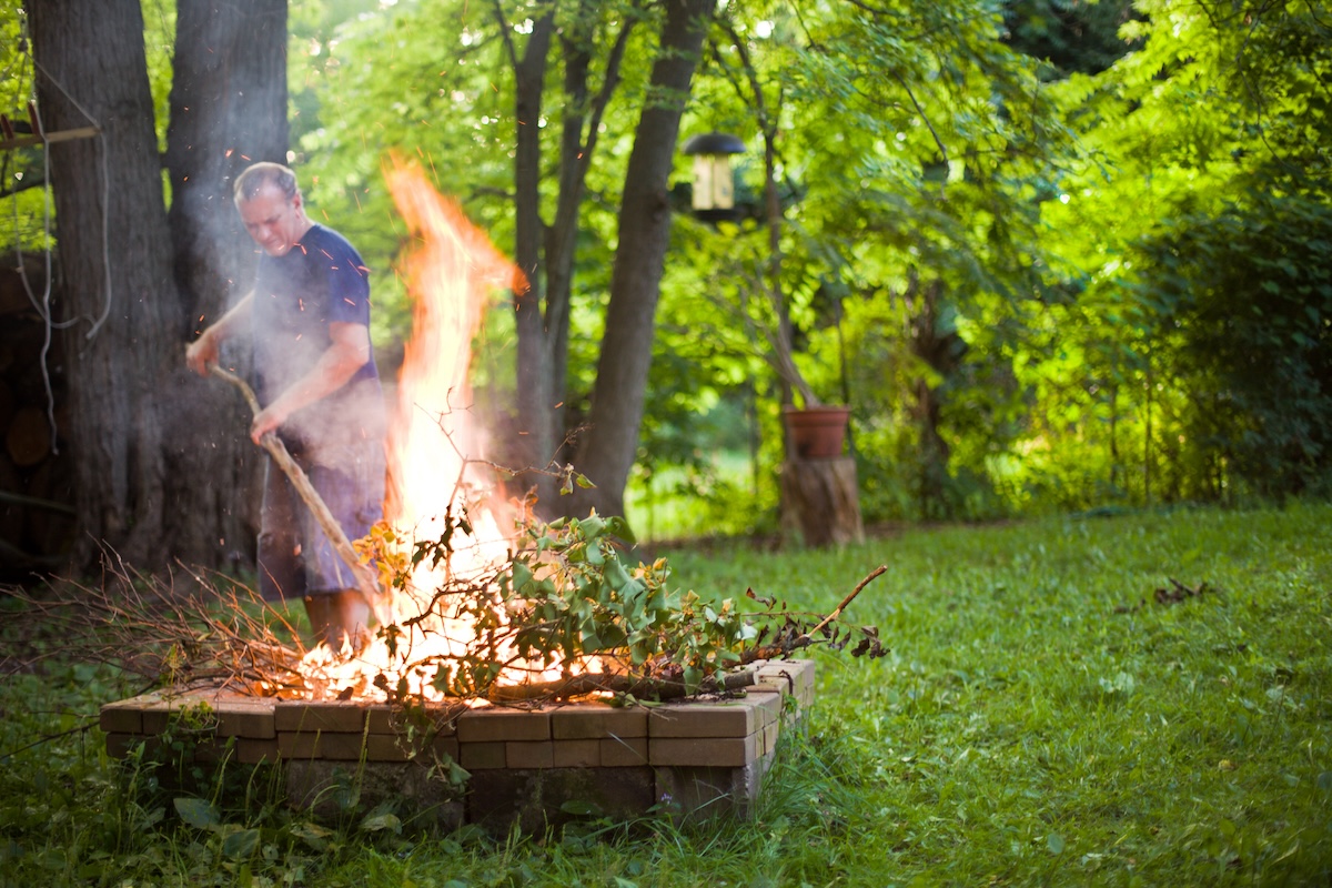 A man wearing a blue shirt tends to a backyard burn pile.