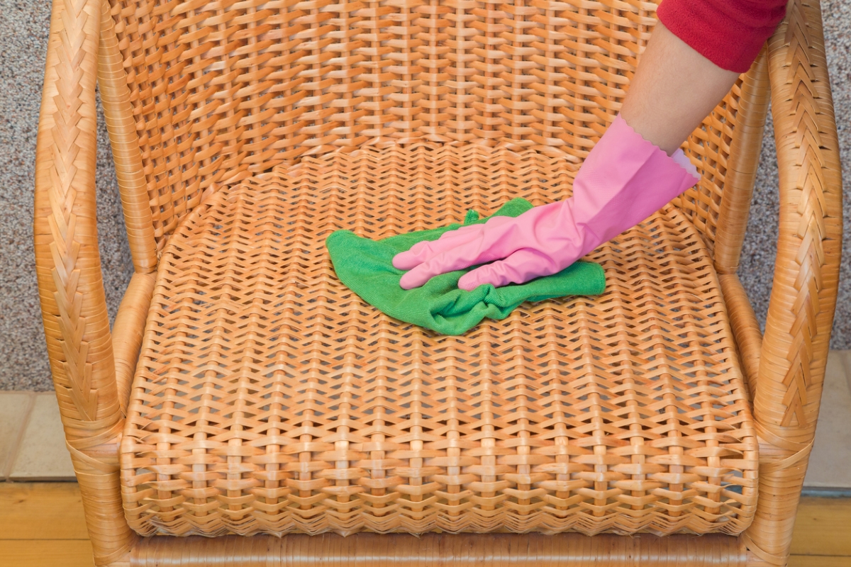 Gloved hand using microfiber towel on wicker chair.