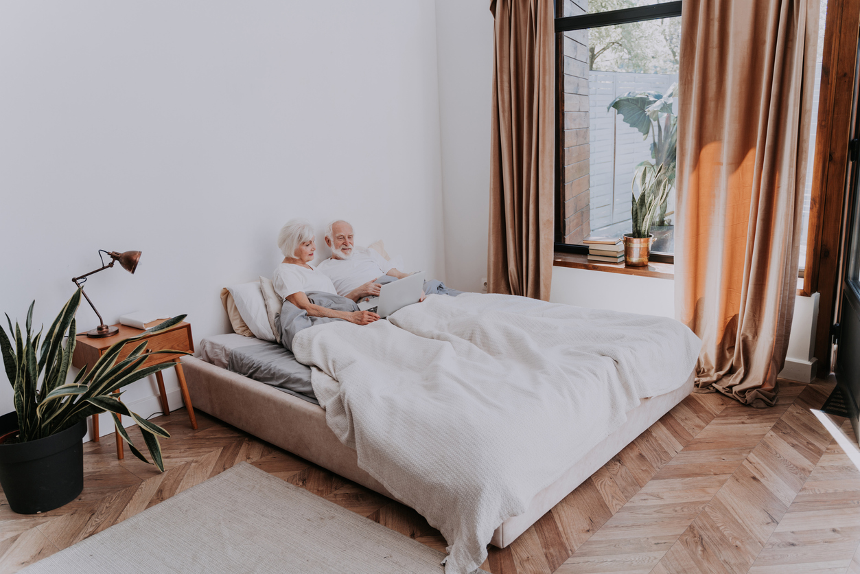 couple de personnes âgées assis dans le lit avec un ordinateur portable dans la chambre à coucher