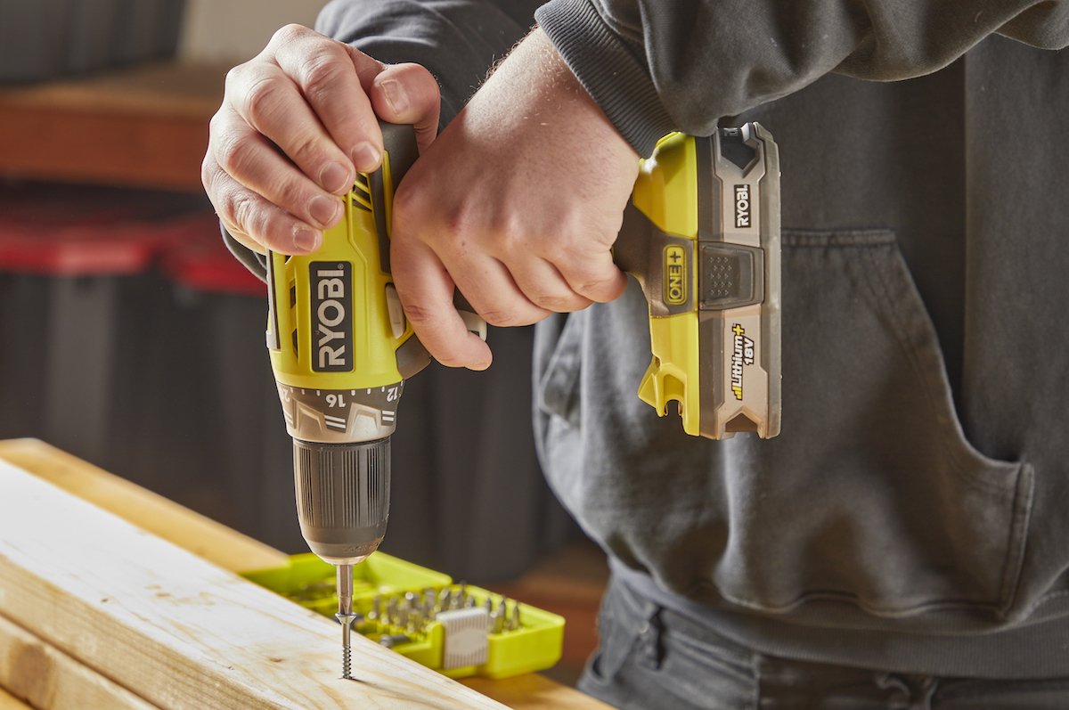 Man uses a drill to drive fastener into a wood board.