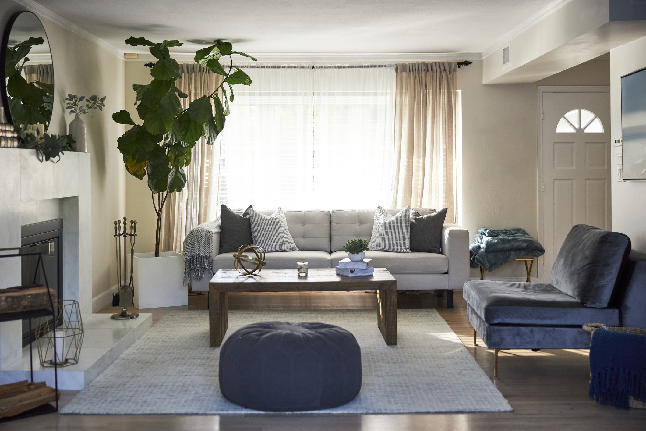 The living room of a suburban home featuring a sofa, easy chair, and bean bag chair is lit by sunlight coming from a large window.