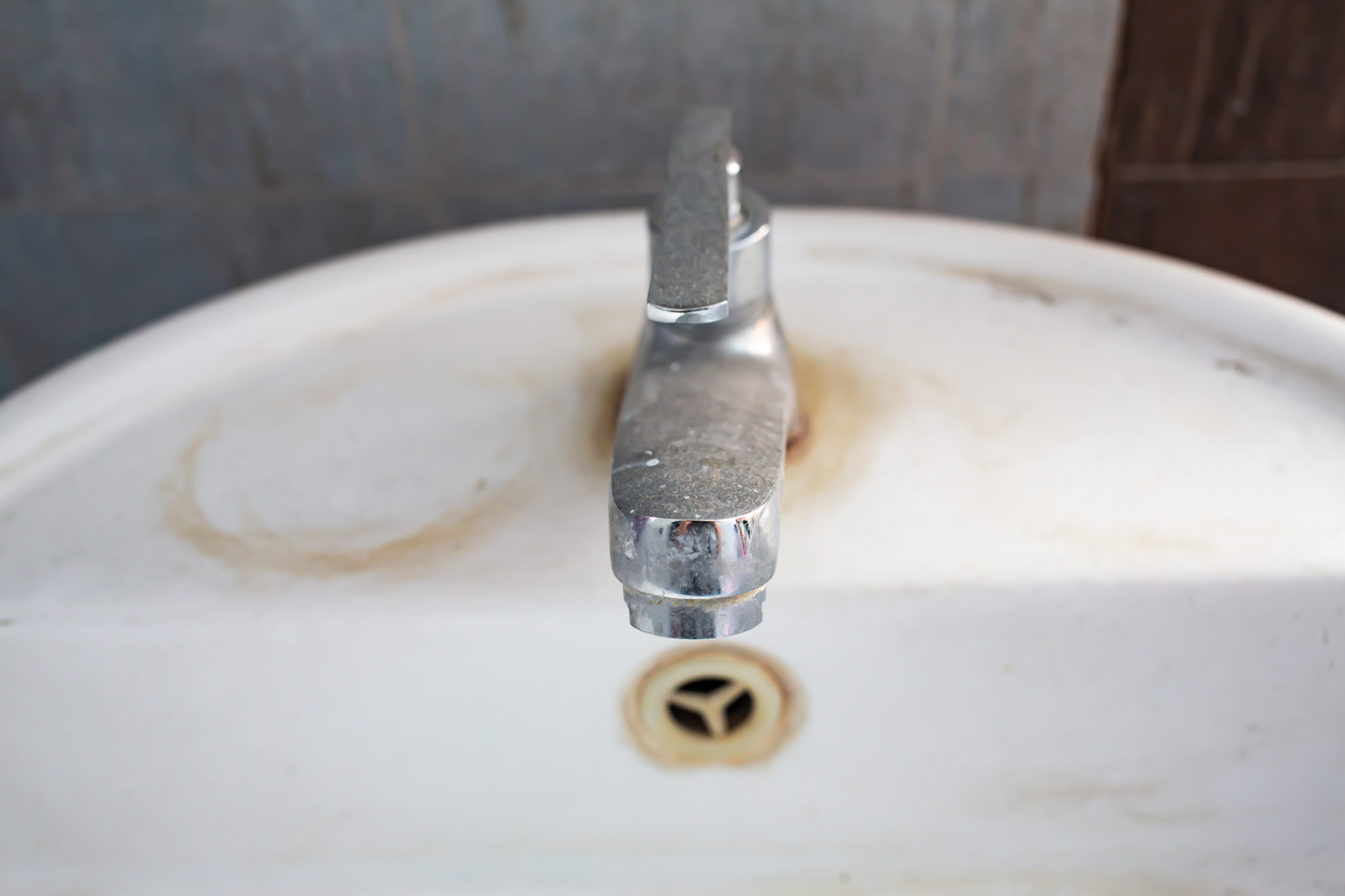 close up on old faucet with rust stains on sink basin