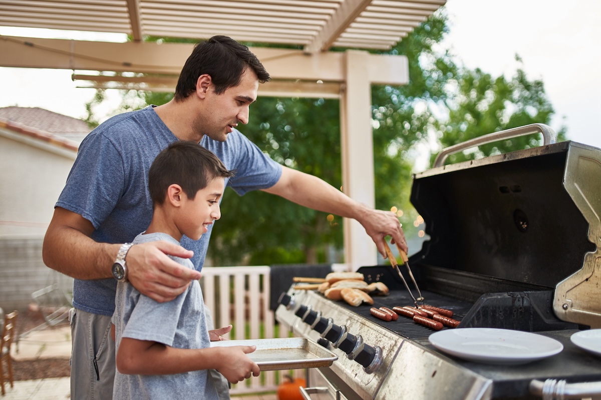 Father teaching son how to grill on outdoor grill.