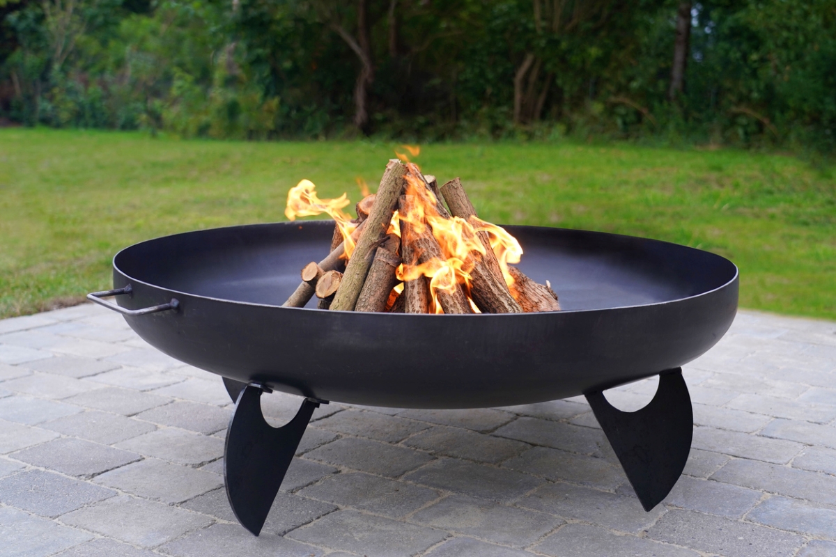 A black metal fire pit is standing on a grey brick patio.