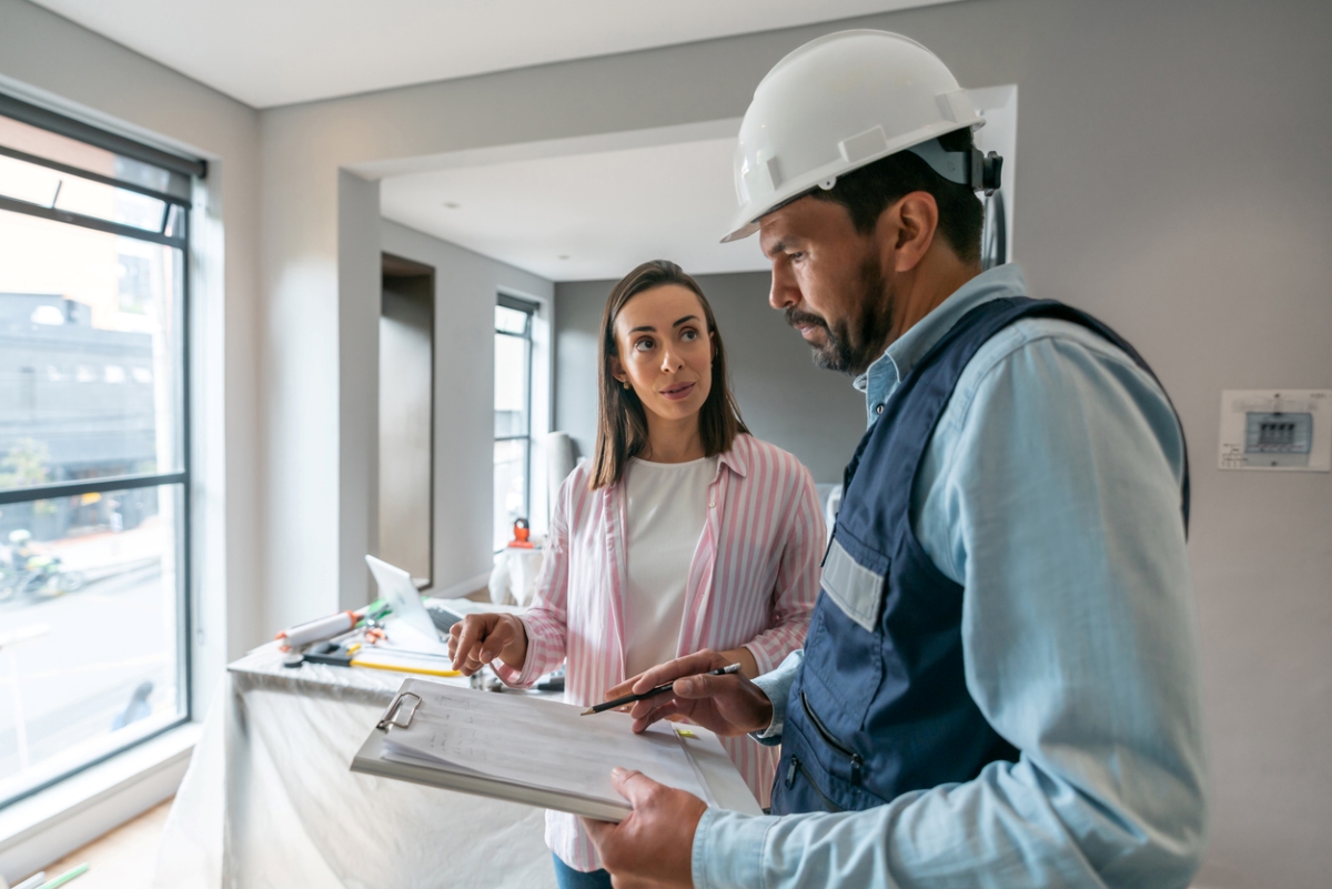 Woman speaking with professional handyman with helmet on.