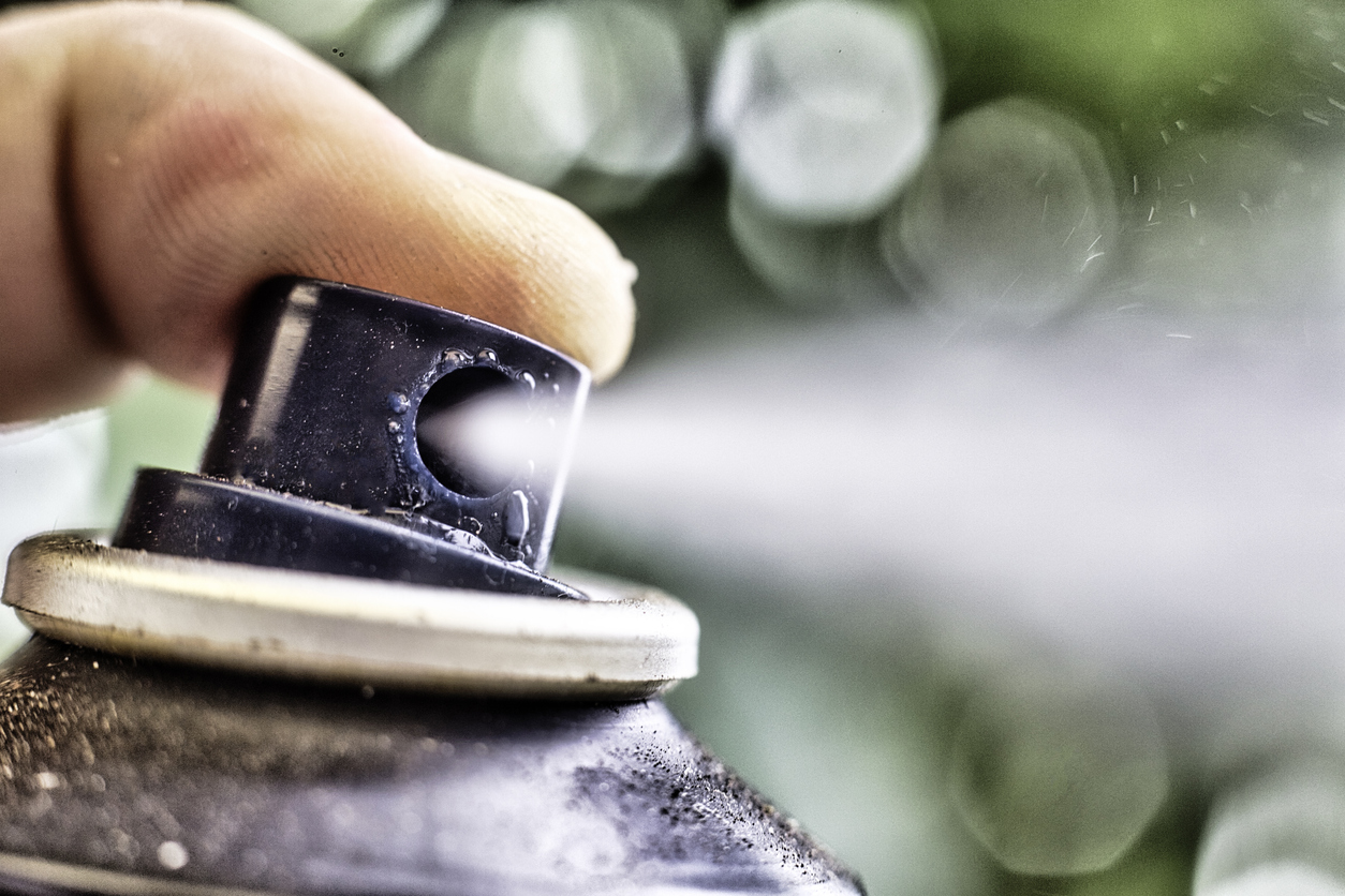 A finger presses the nozzle on an aerosol can causing a spray.