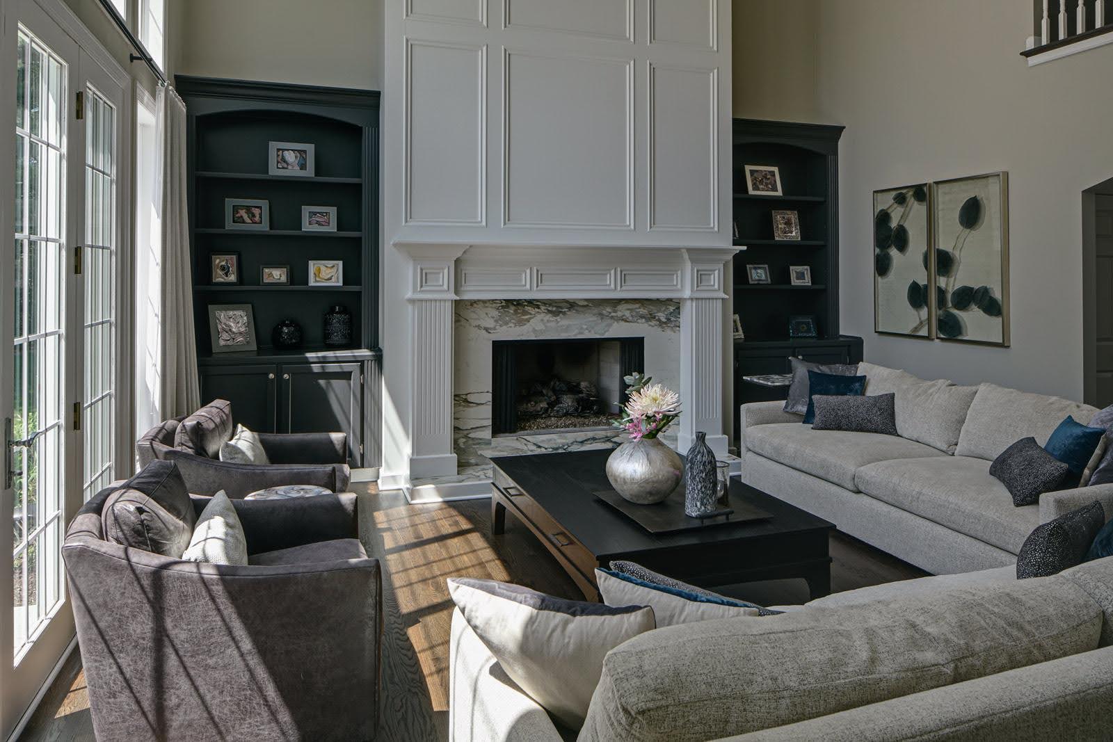 A large, traditional sitting room full of long sofas, easy chairs, and a coffee table are positioned around a marble fireplace.