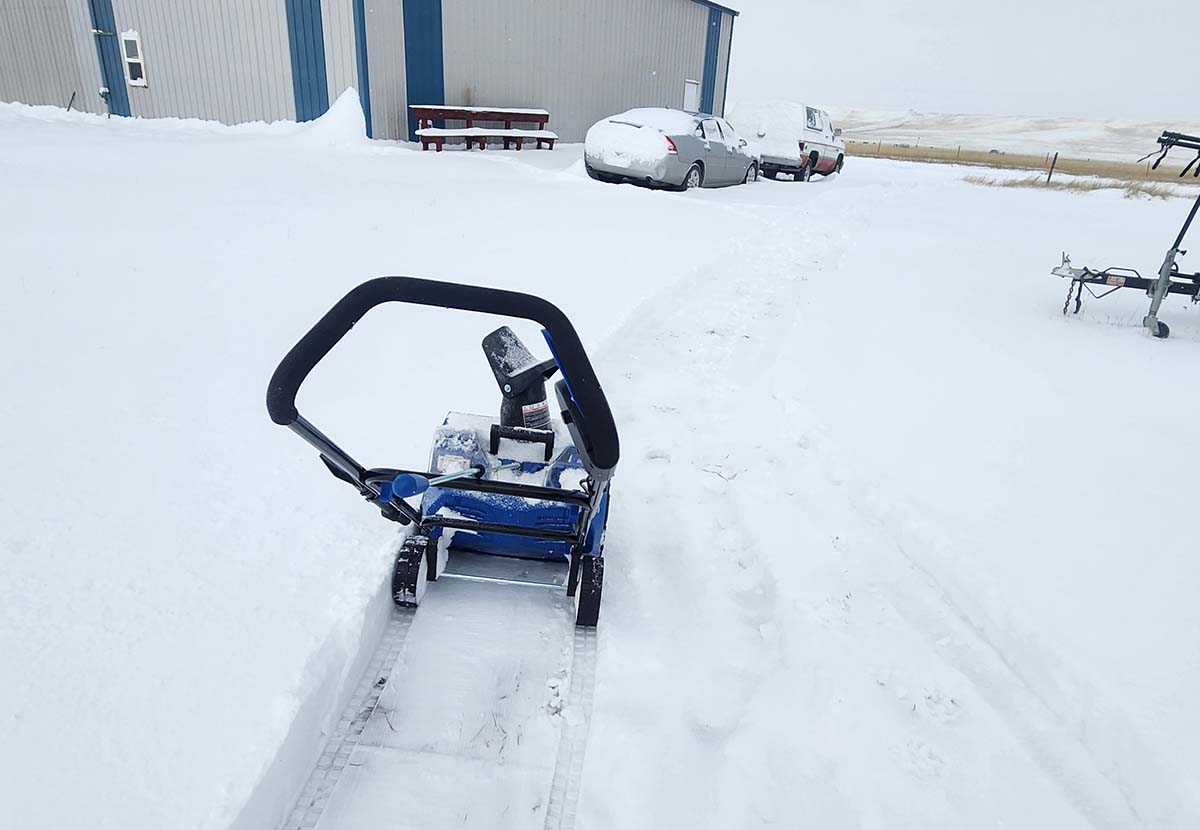 The Snow Joe Single-Stage Snow Blower clearing a path through snow covering a large cement surface.