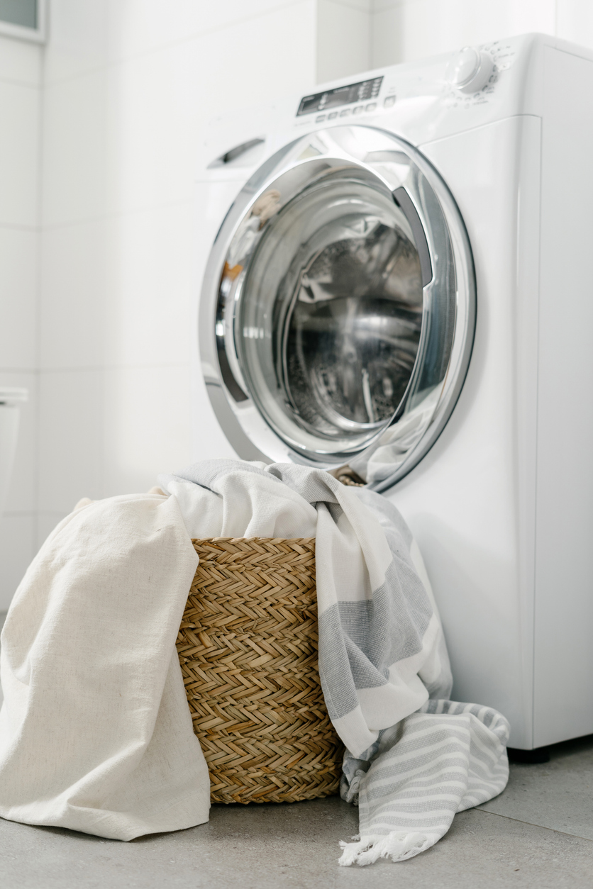 white and grey sheets in wicker basket sitting in front of laundry machine