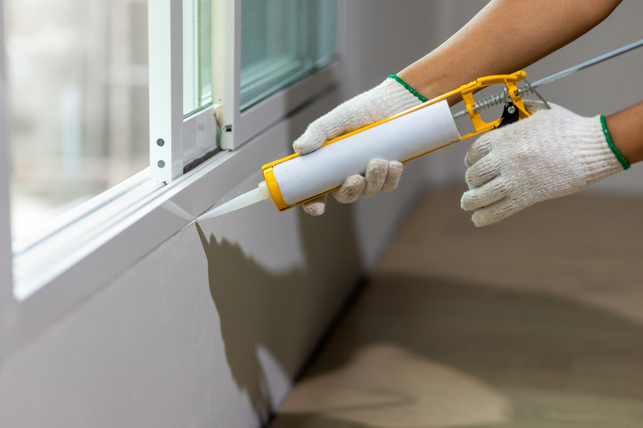 Person wearing construction gloves sealing a window with caulk sealant.