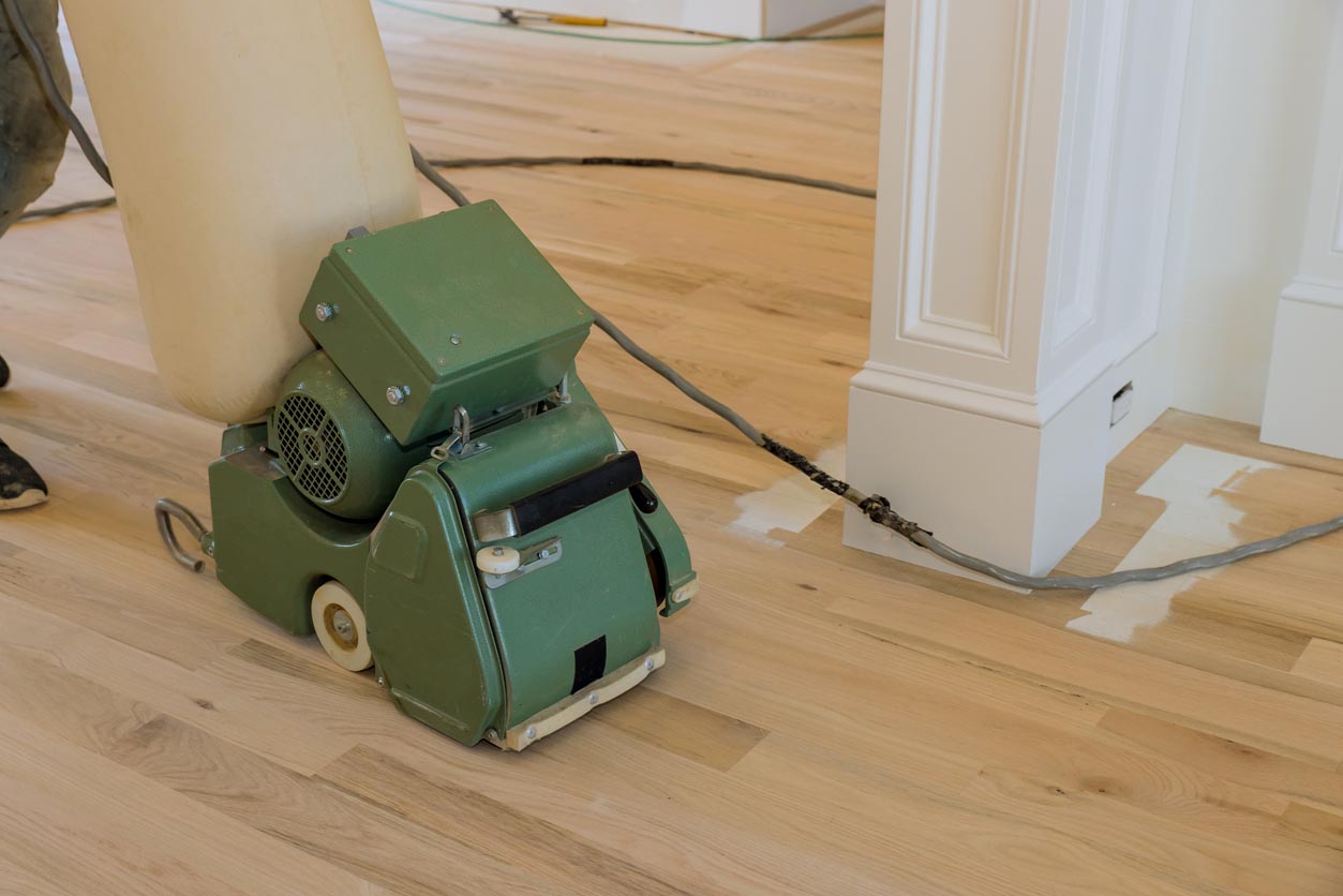 A floor sanding machine in the process of sanding hardwood floors in a home.