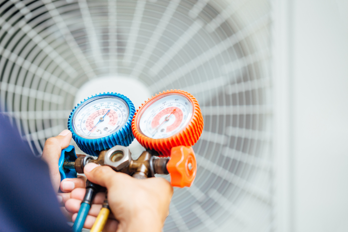 Un technicien en climatisation utilise un outil de jauge pour tester un climatiseur extérieur.