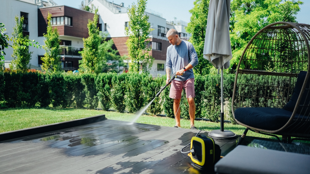 Mature man cleaning the patio decking with a pressure washer.