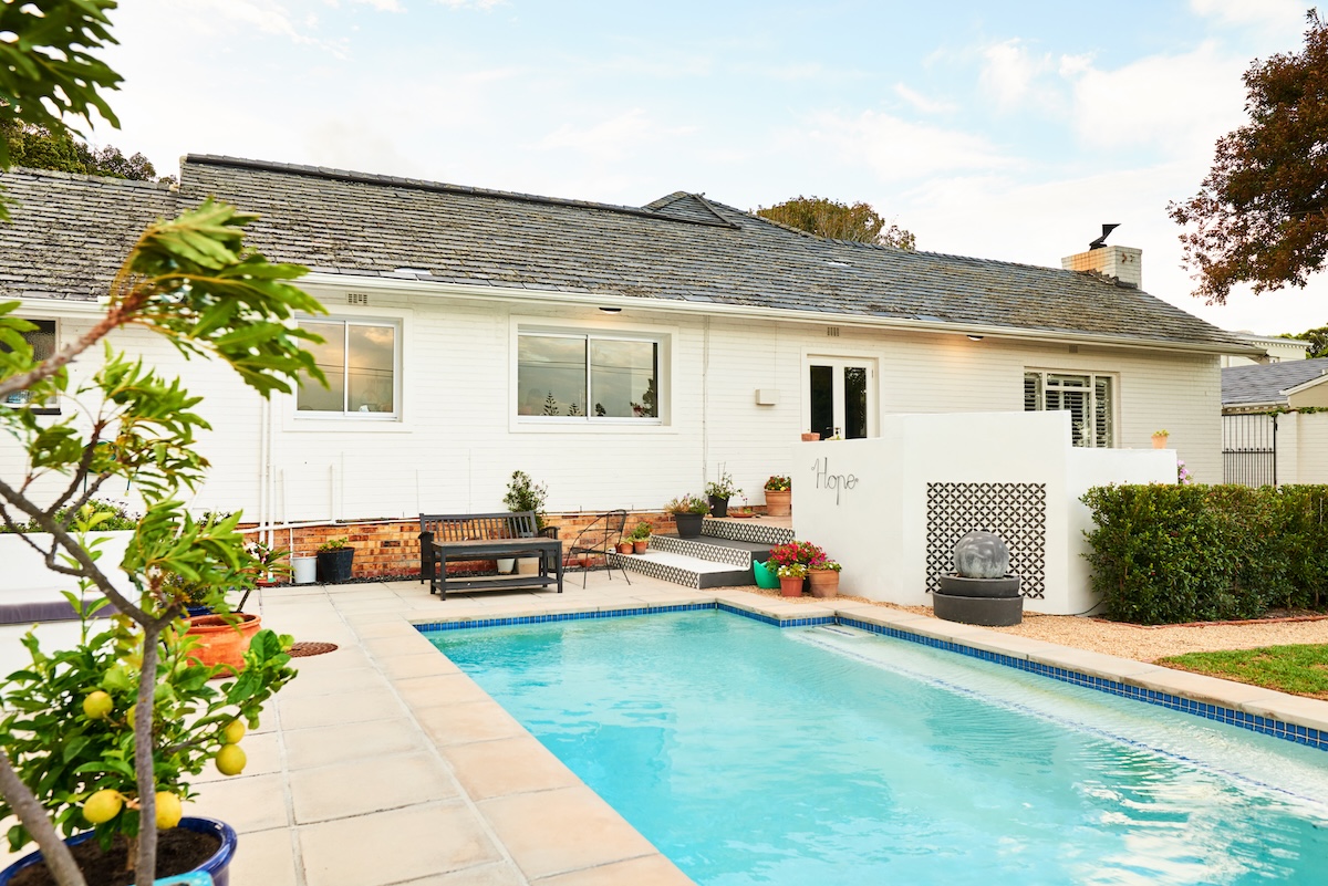 White ranch style home with a small swimming pool in the backyard.