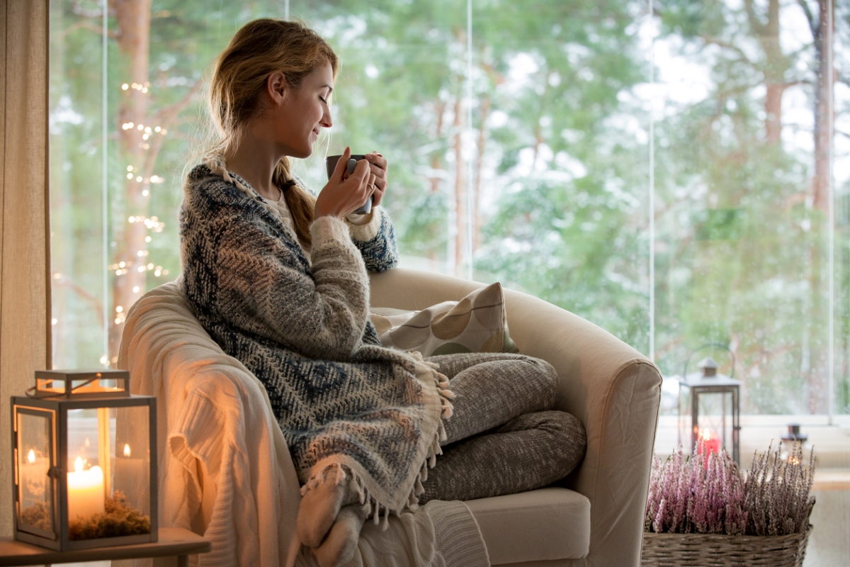 Young woman sitting by window with hot drink.