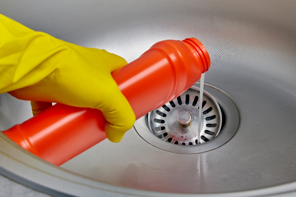 Pouring cleaner down kitchen sink drain.