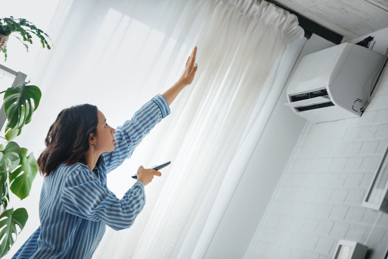 femme dans un salon moderne et lumineux près d'une fenêtre blanche avec rideaux, met en marche la climatisation montée sur le mur