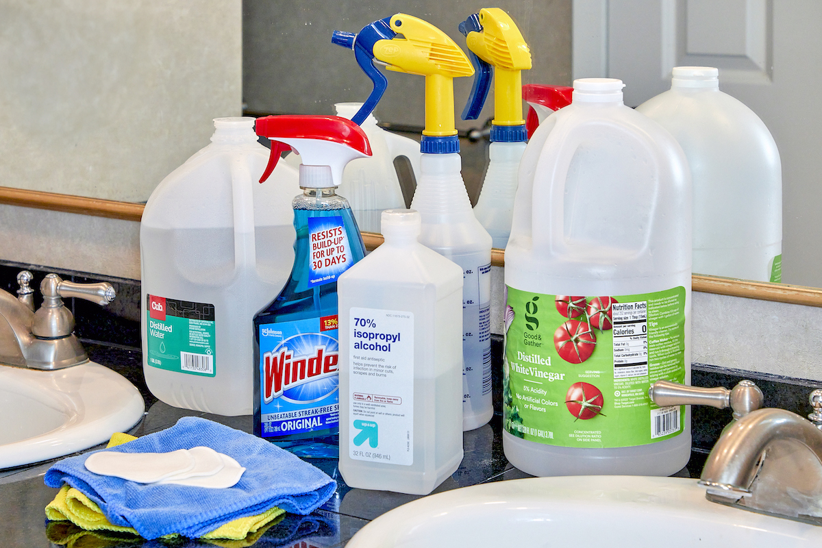 Materials needed to clean a mirror, including vinegar, rubbing alcohol, and microfiber cloths.