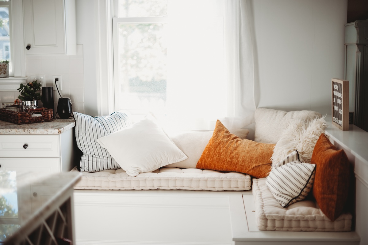 Siège de fenêtre confortable avec coussins orange et blancs avec rangement en dessous.