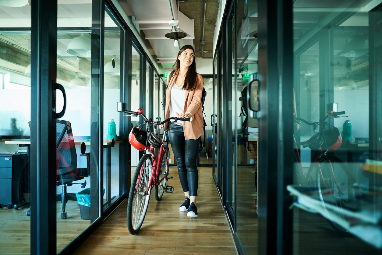 Young businesswoman pushing her bicycle and passing cubicles in the office