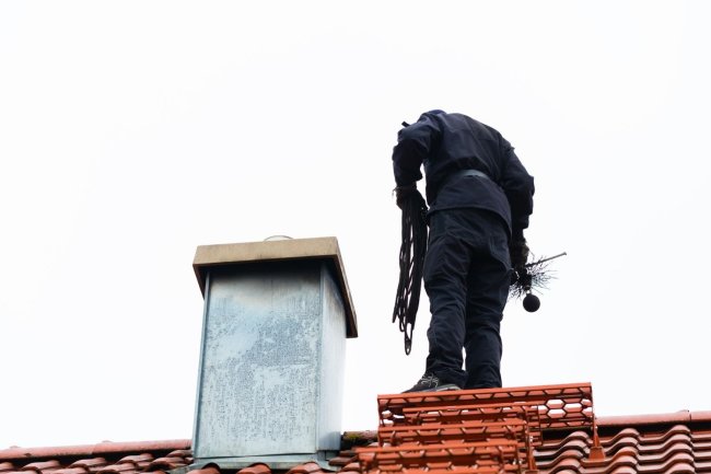 Un ouvrier vêtu de noir se tient sur un toit de tuiles rouges.