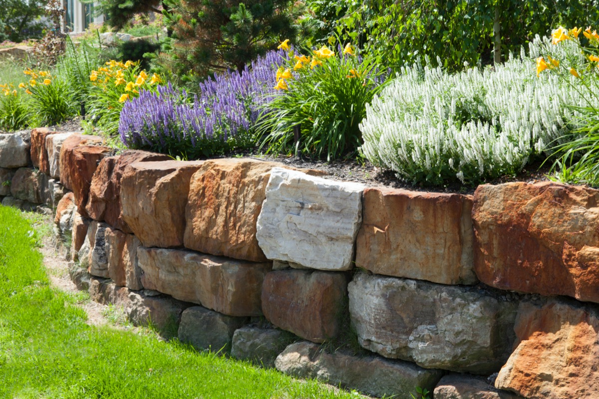 A flower bed atop a bed made of multicolored stones in a retaining wall.