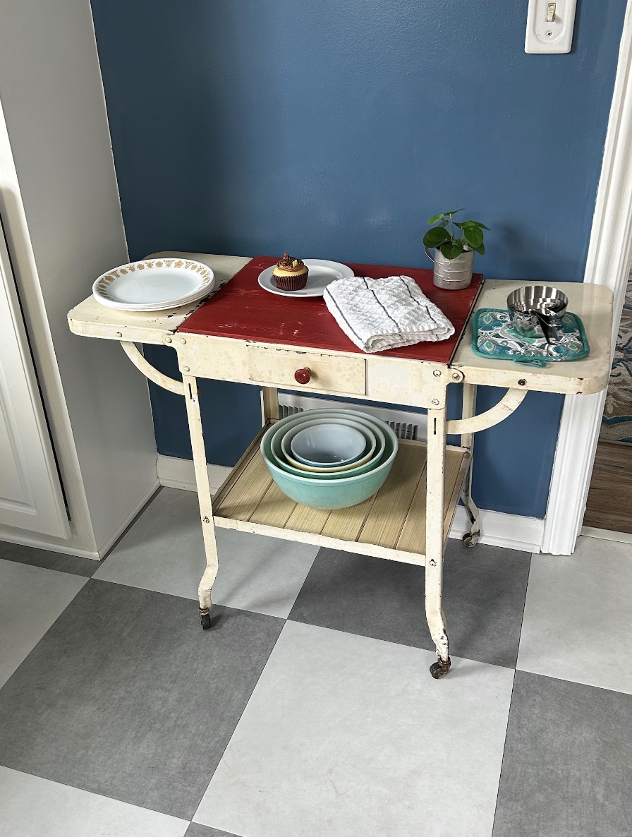 A vintage ivory kitchen cart set with plates, bowls, and napkins.