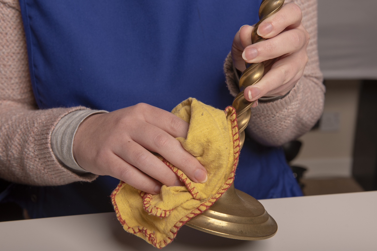 Woman with blue sweater polishing brass candle sticks with yellow cloth.