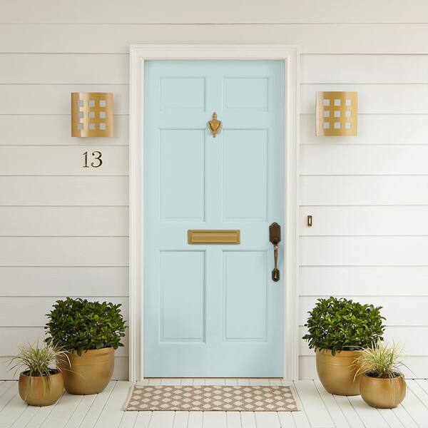 On the porch of a white house two plants sit on either side of a pale aqua colored door.