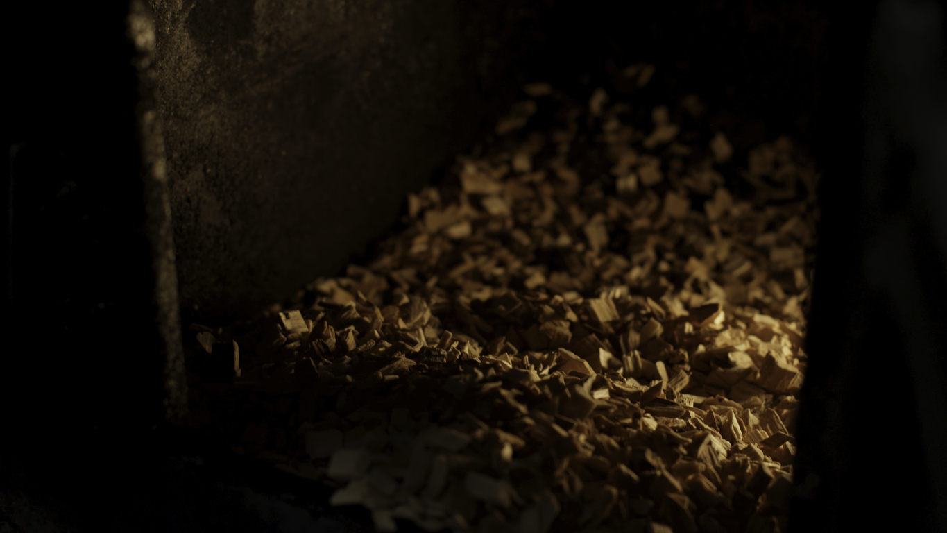 A man puts sawdust in a cast iron furnace close-up. Man's hands putting wood into the fire close up. Wood furnace. Open firebox with a hardwood log laid inside a furnace. Flames and an ember are visible in a blurry background.