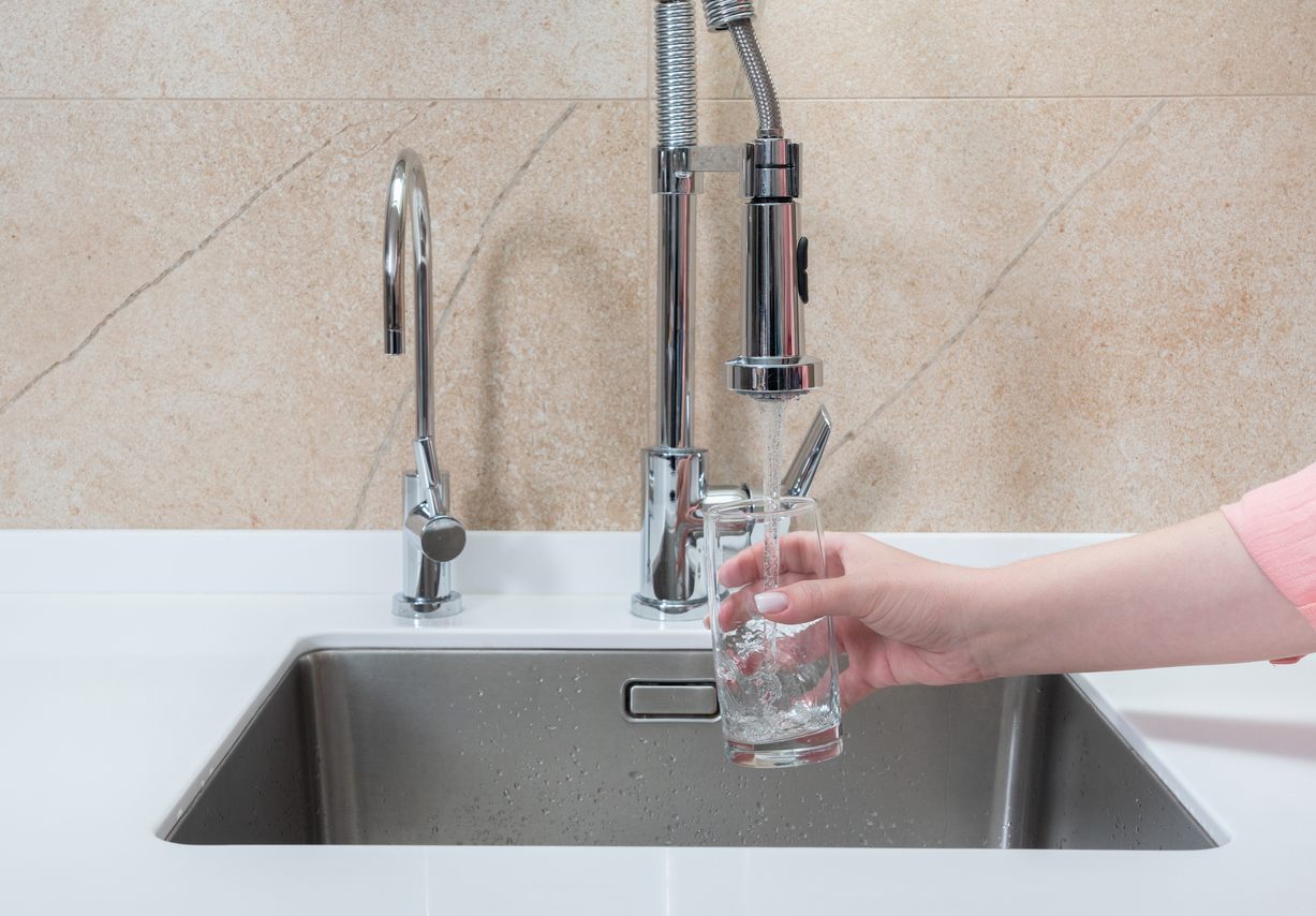 Main de femme tenant une tasse sous l'eau courante d'un robinet à bec extractible et à béquille