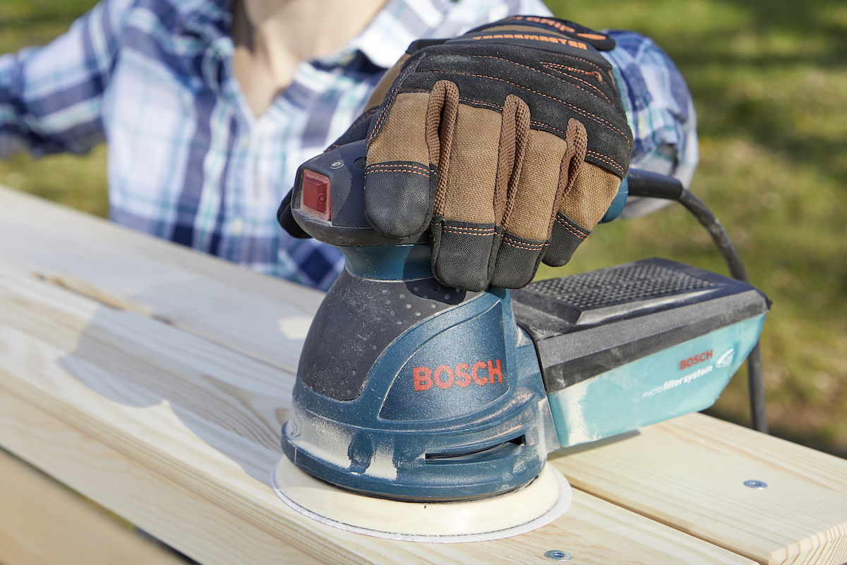 Close view of a palm sander in a woman's gloved hand.