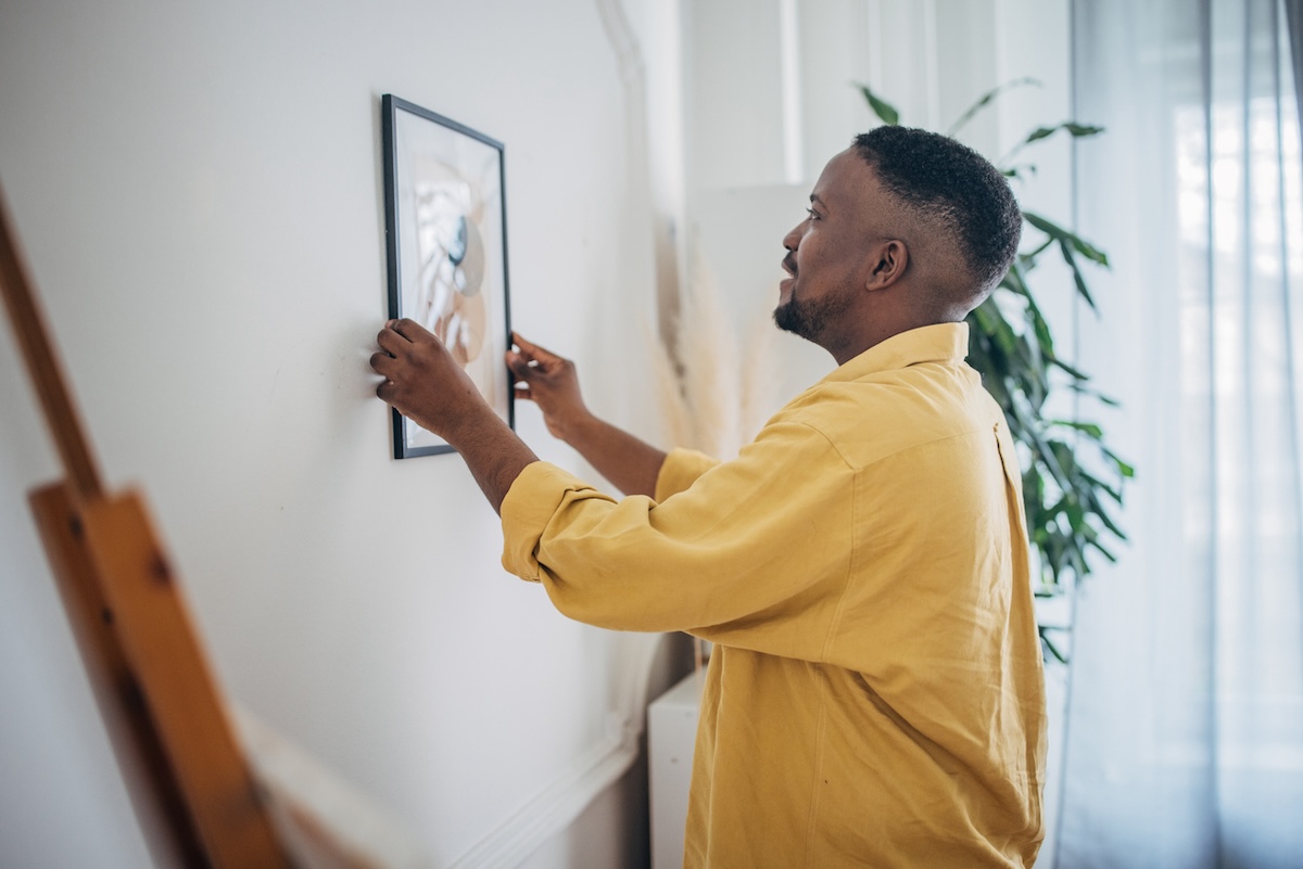 Un homme accroche un tableau encadré sur le mur du salon.