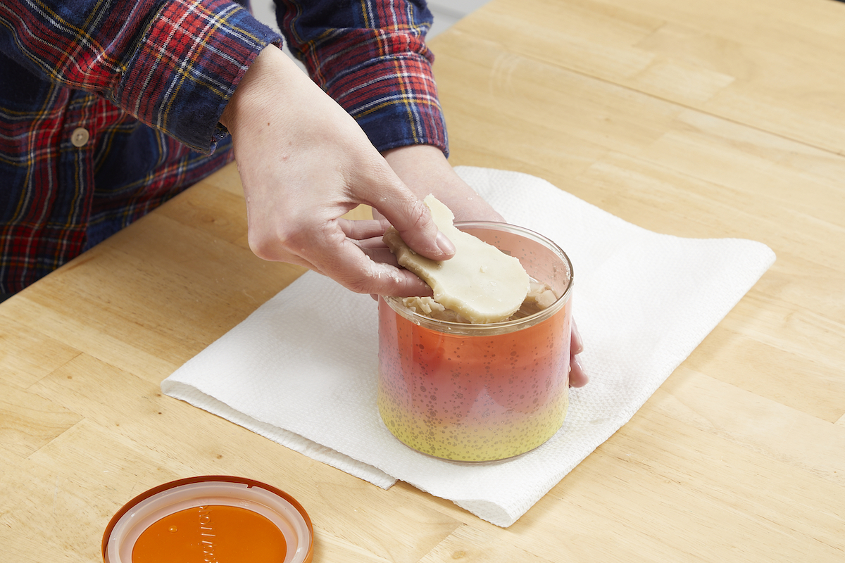 Woman removing clumps of wax from a candle jar with her fingers.