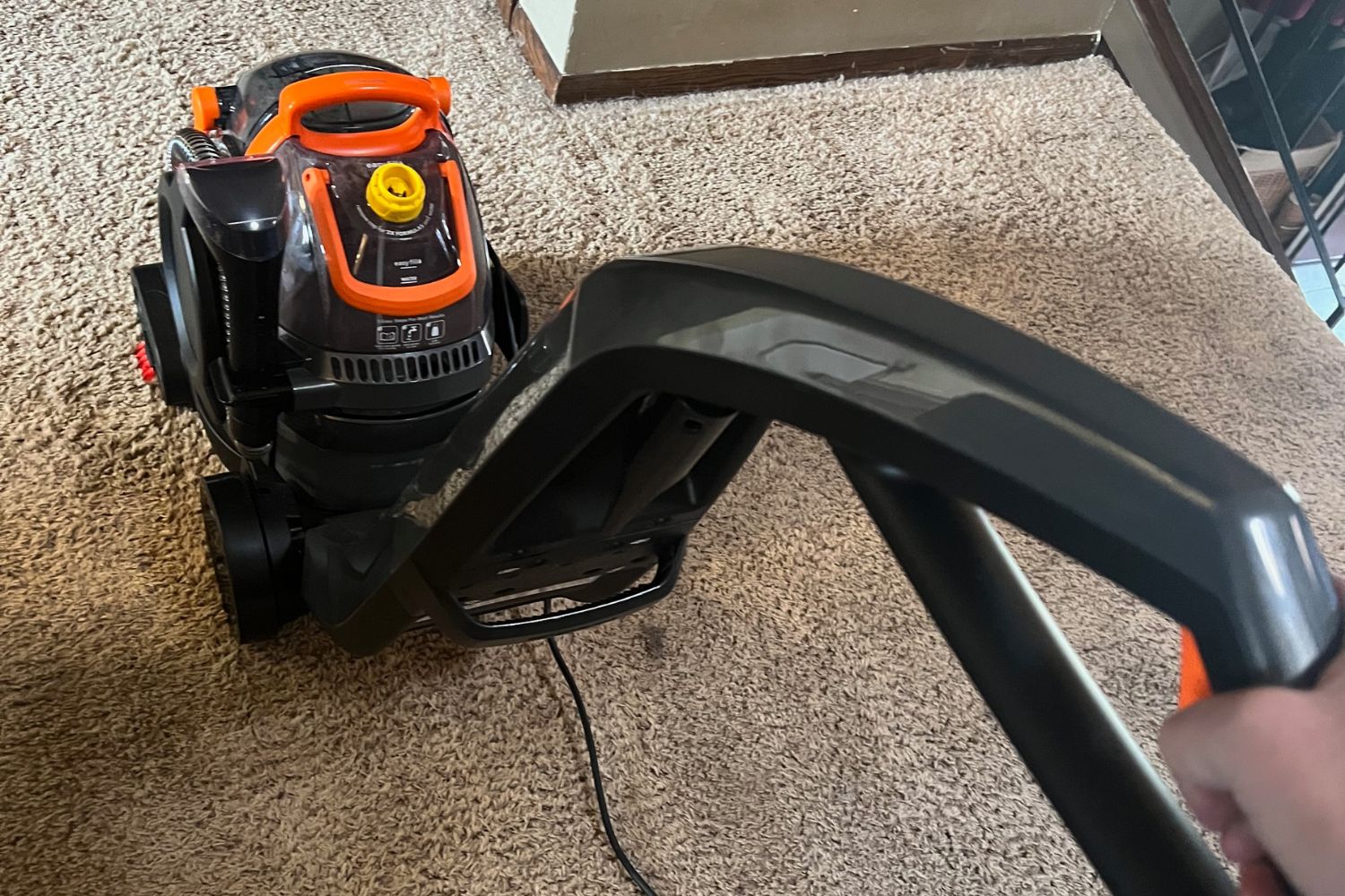 Person pushing gray and orange carpet cleaner across tan carpet