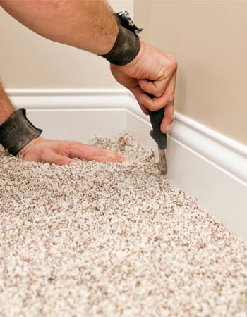 A close up of a person cutting a beige carpet to fit the area of the floor.