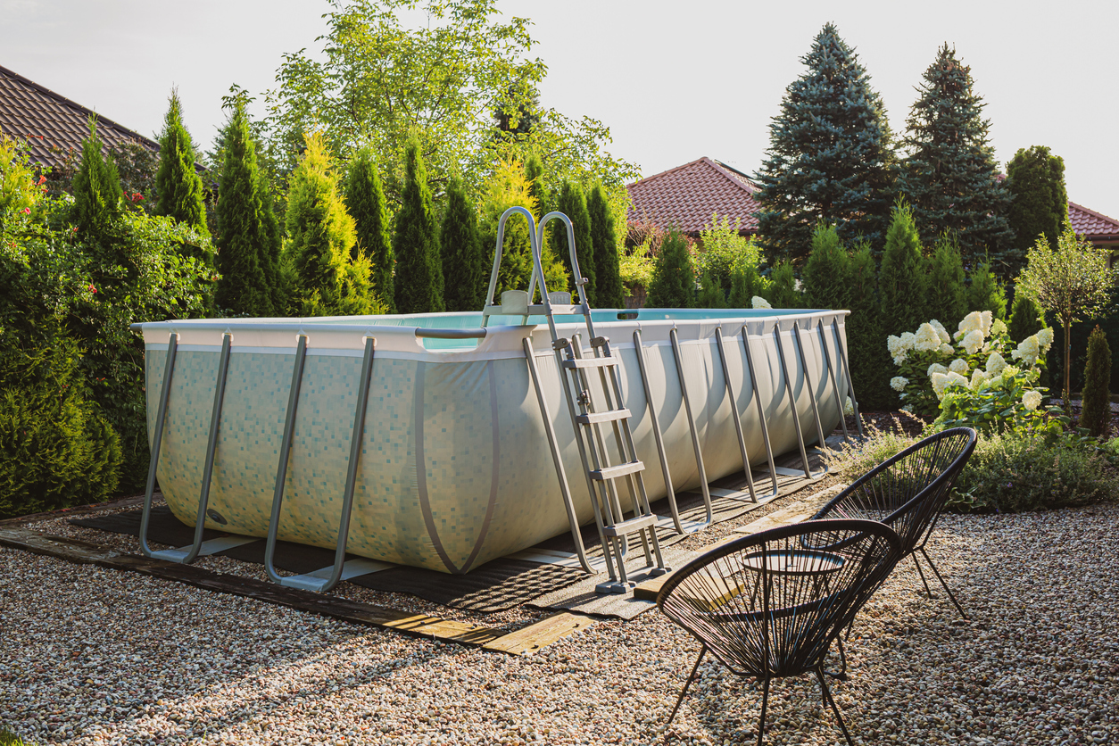 Piscine longue, hors sol, rectangulaire, à crémaillère, en plein air, dans un coin de jardin en galets. Vacances d'été et loisirs.