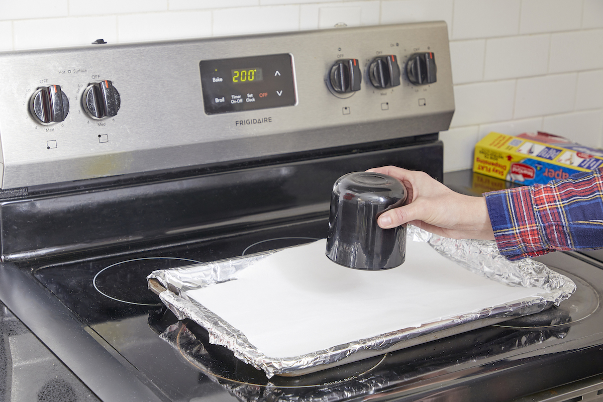 Woman inverts candle jar onto parchment paper to put in oven.