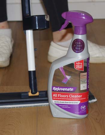 A spray bottle of the Rejuvenate All Floors Cleaner next to a mop during testing to clean a wood floor.