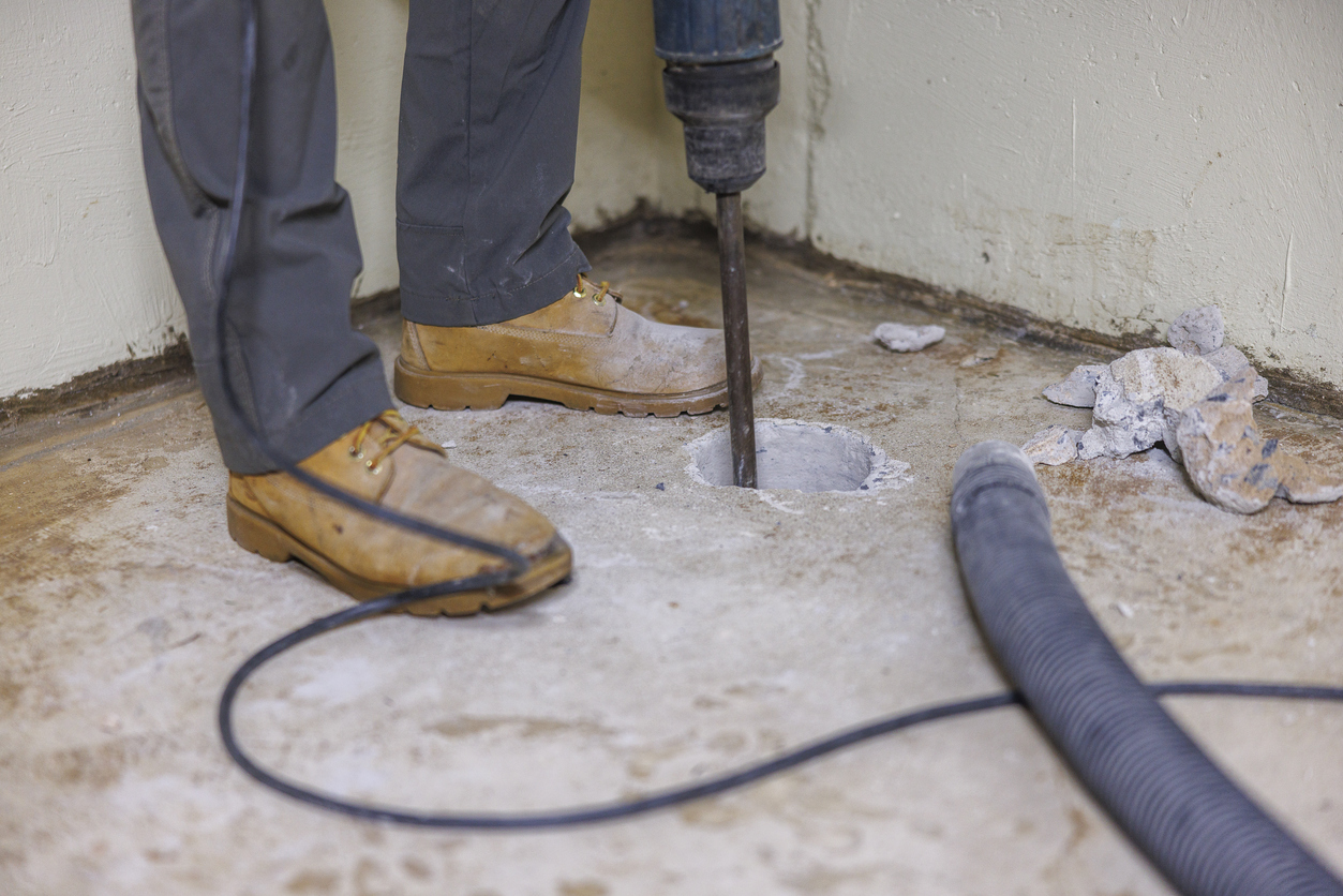 Radon mitigation system installation. A worker is drilling a hole in the basement floor to improve the house.