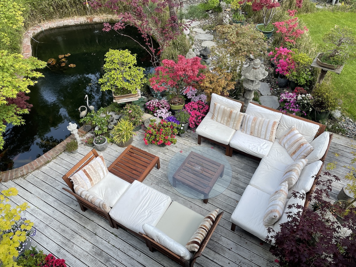 Terrasse extérieure avec mobilier blanc et plantes colorées près d'un étang à carpes koï.