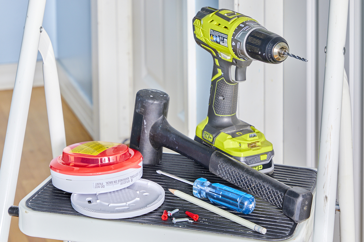 Smoke detector and installation tools sitting on a step ladder.