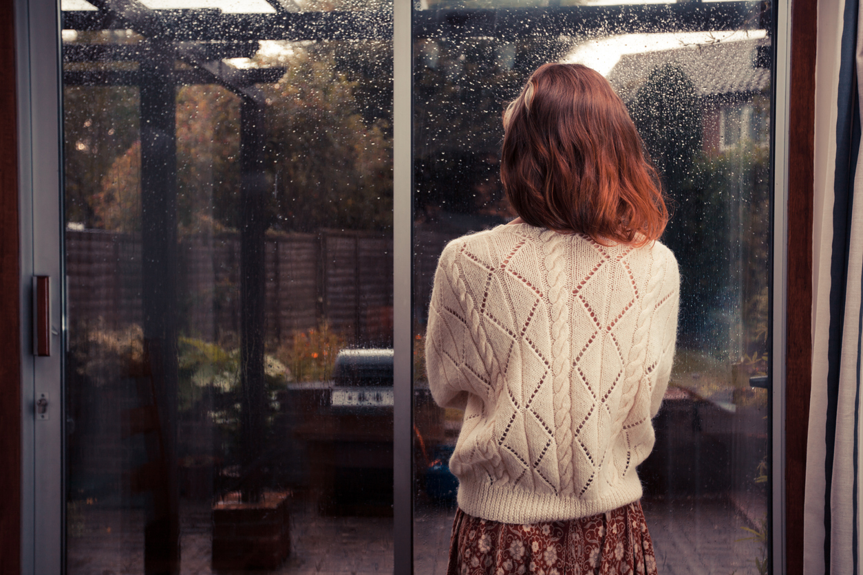 Jeune femme debout près d'une fenêtre regardant la pluie à l'extérieur